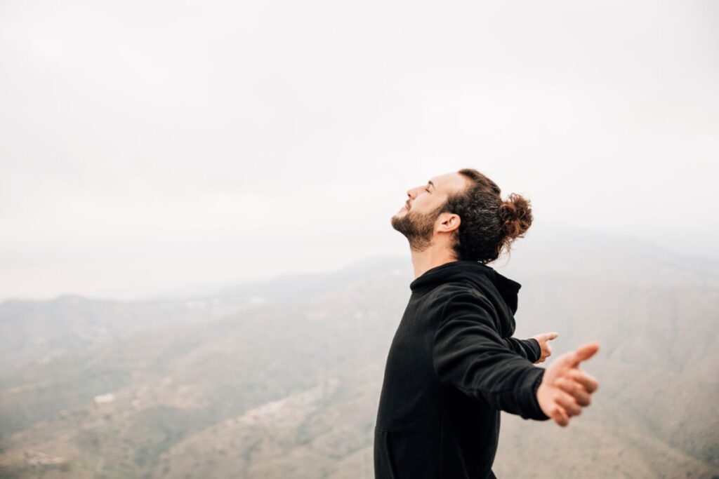 A man stands on a mountain with arms wide open, symbolizing a life worth living.